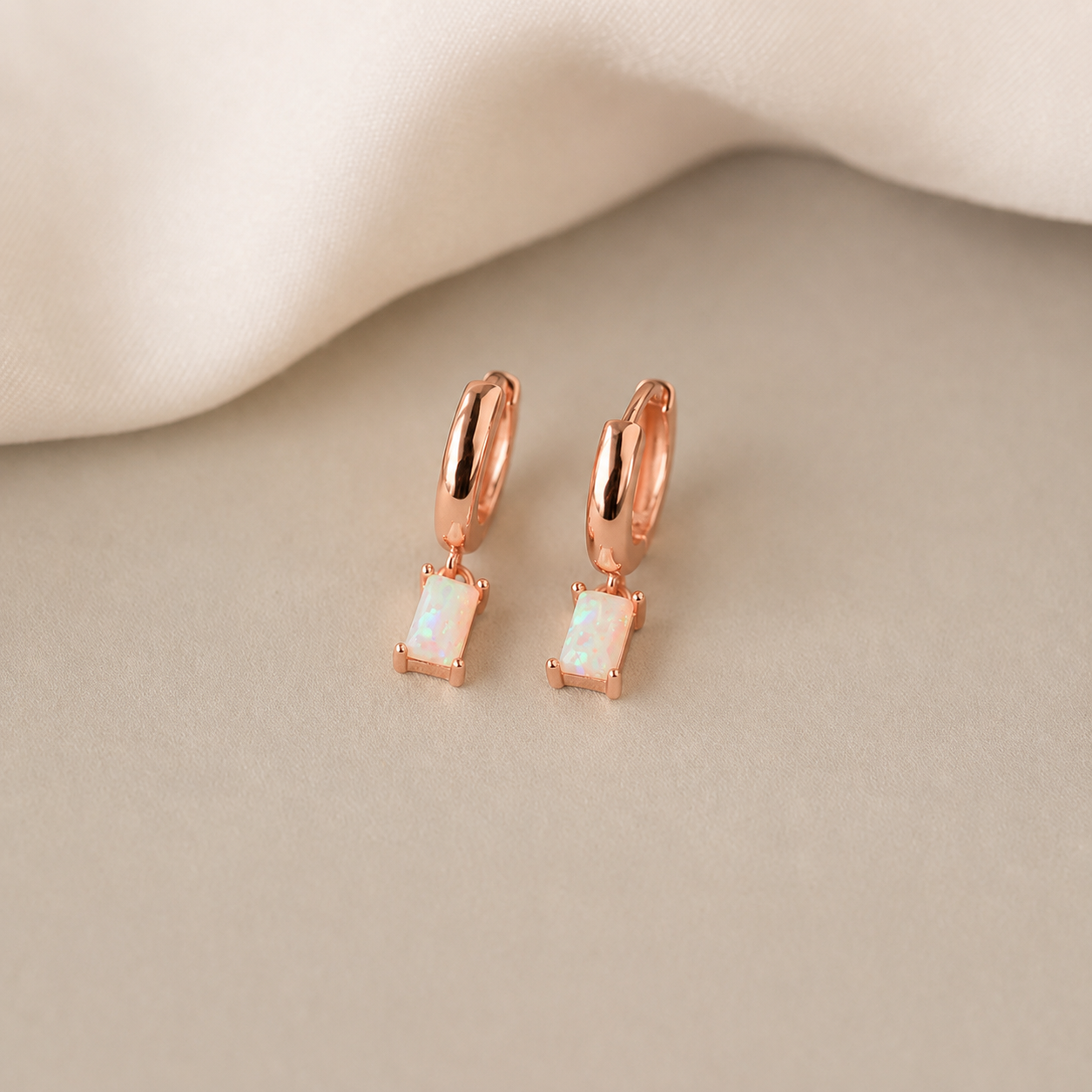 Rose gold hoop earrings with square gemstones on a beige surface